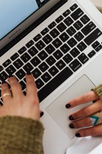 Na zdjęciu widoczne są dwie dłonie, które piszą na klawiaturze laptopa.