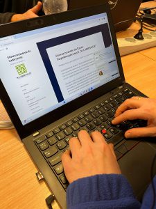 Zdjęcie przedstawia laptop, na ekranie otwarta jest strona internetowa Stowarzyszenia na Rzecz Niepełnosprawnych "W LABIRYNCIE". Na zdjęciu widać również ręce osoby, która używa klawiatury laptopa.