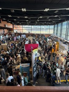 Duża hala targowa widziana z góry, wypełniona tłumem i stoiskami. W centrum wyróżnia się stoisko „Lavazza”. Widać alejki, kolejki oraz banery palarni kawy.